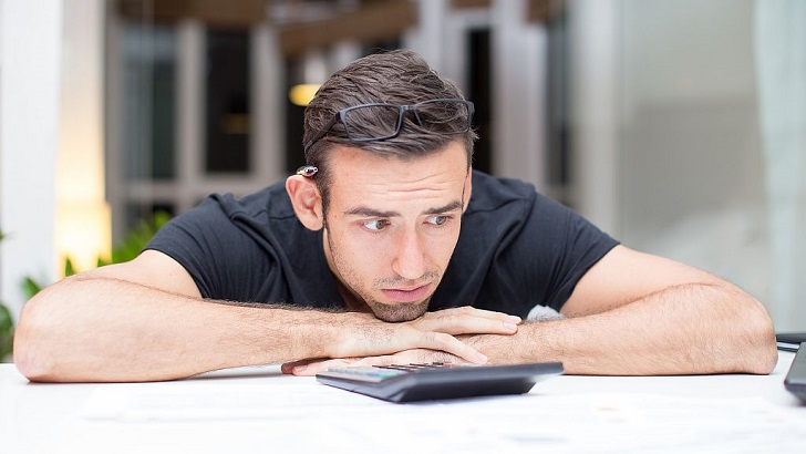 Frustrated Man Lying on Desk With Calculator