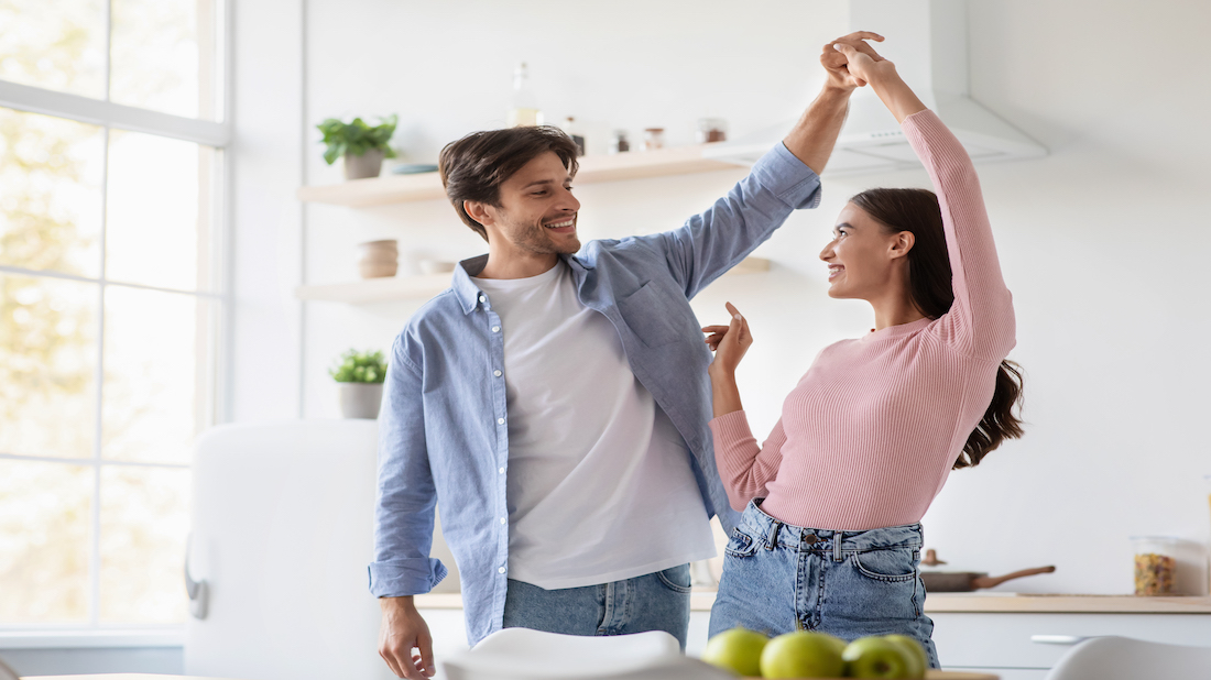 Happy cheerful attractive young husband and wife dancing and have fun together in kitchen interior